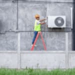 addetto su una scala con dispositivi di sicurezza che controlla il motore di un condizionatore